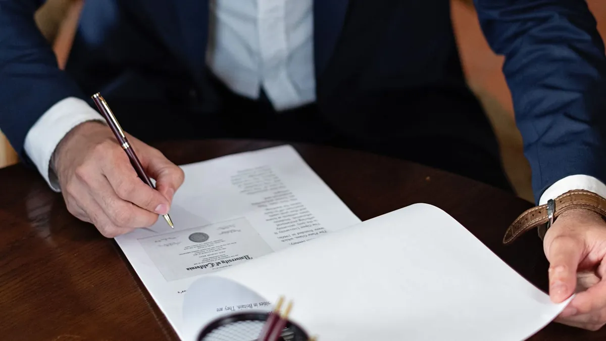 Personne en veston qui signe un document sur une table en bois