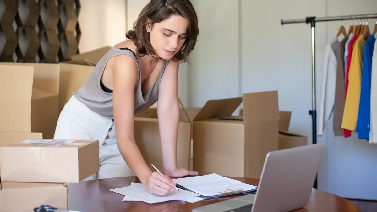 Entrepreneure qui prend des notes devant son ordinateur portable, entourée de boîtes de déménagement
