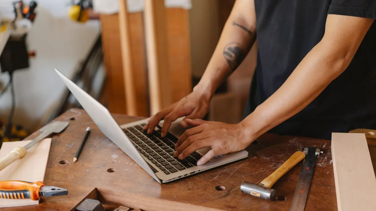 Artisan qui travaille sur son ordinateur portable à son établi, entouré d’outils