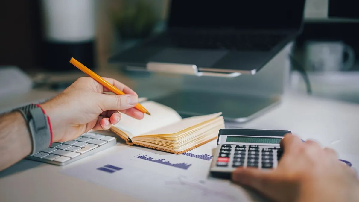 Mains qui prennent des notes et utilisent une calculatrice devant un ordinateur portable